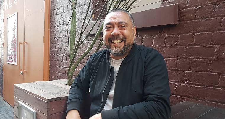 Poni Sula smiling, seated outside a bar